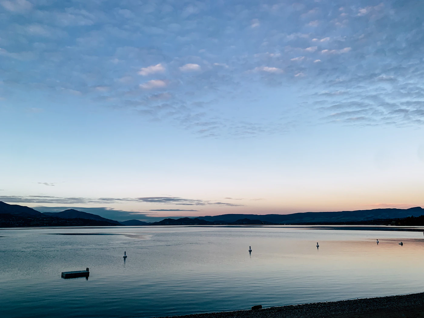 A solitary boat drifting across the serene morning waters of Okanagan Lake