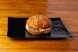 A hamburger on a black plate on a wooden table