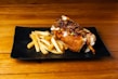 A black plate topped with a piece of meat and french fries