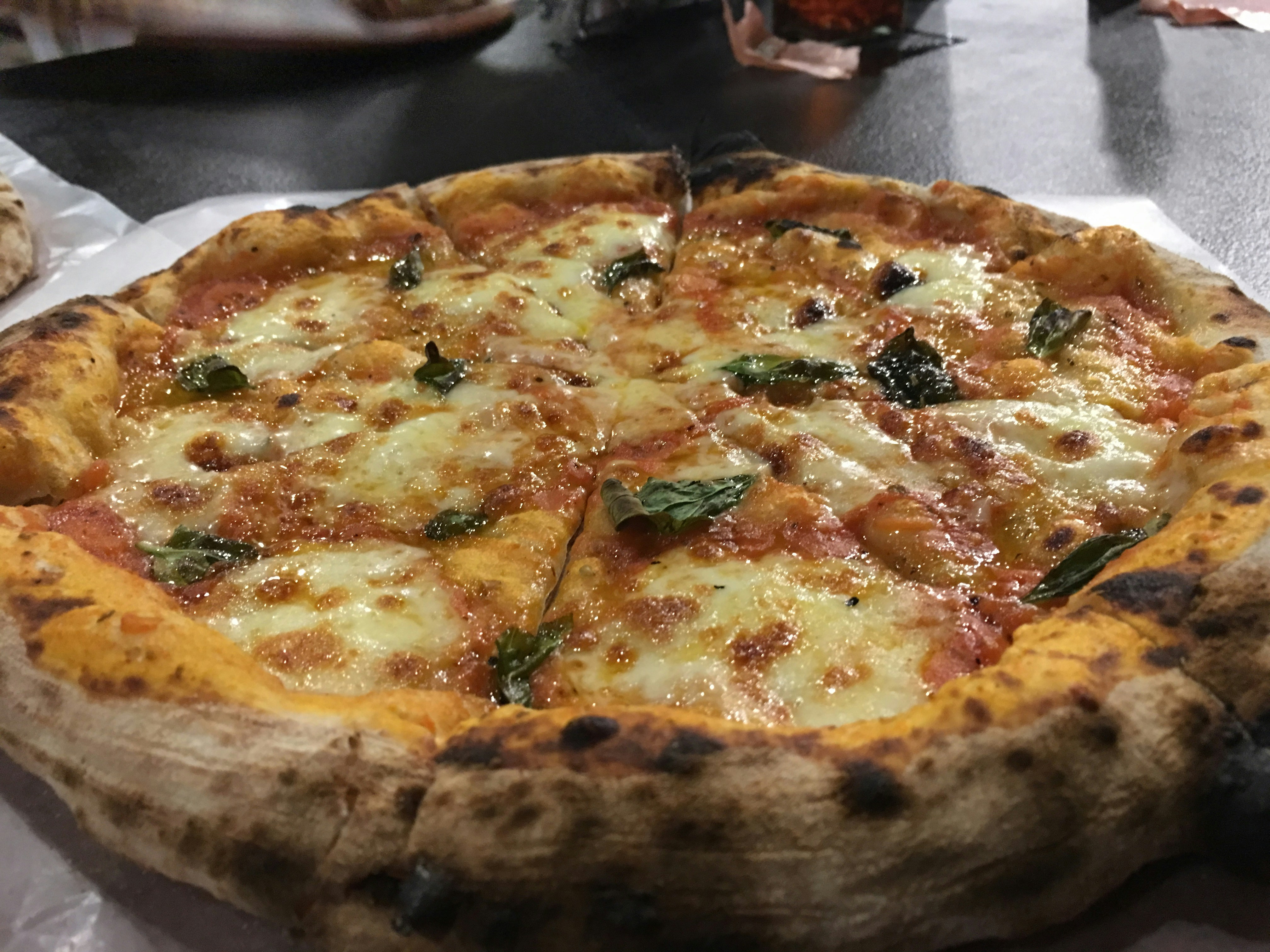 Artisan pizza with golden crust, fresh mozzarella, basil leaves on dark wooden surface with moody low lighting