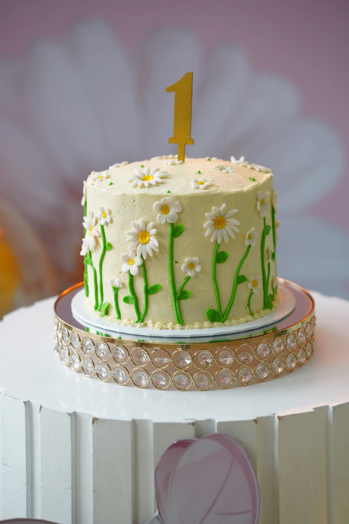 A small pale cake with piped daisies and a single candle.