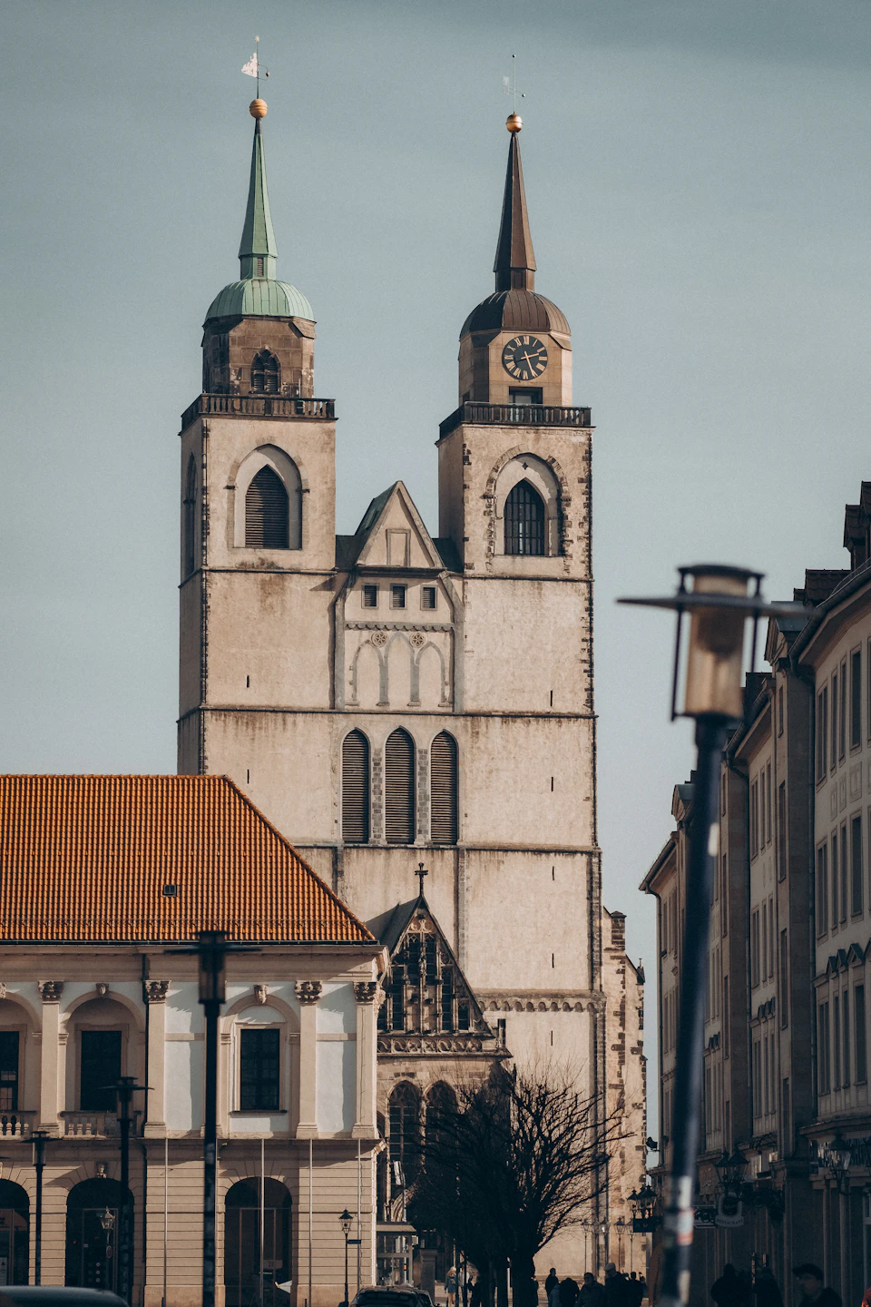 Large white church with two tall spires and clock tower dominates city street corner scene
