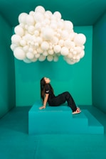A woman laying on top of a blue platform under a bunch of white balloons