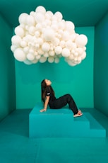 A woman laying on top of a blue platform under a bunch of white balloons