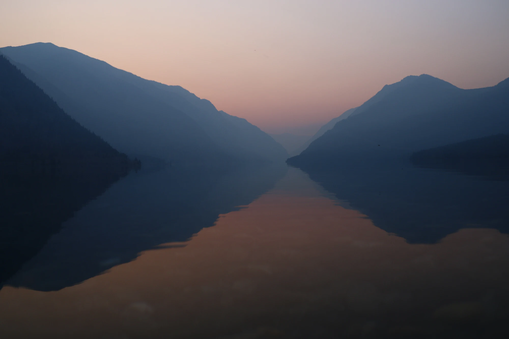 Un lac de montagne au lever du jour, parfaitement lisse, entre deux versants.