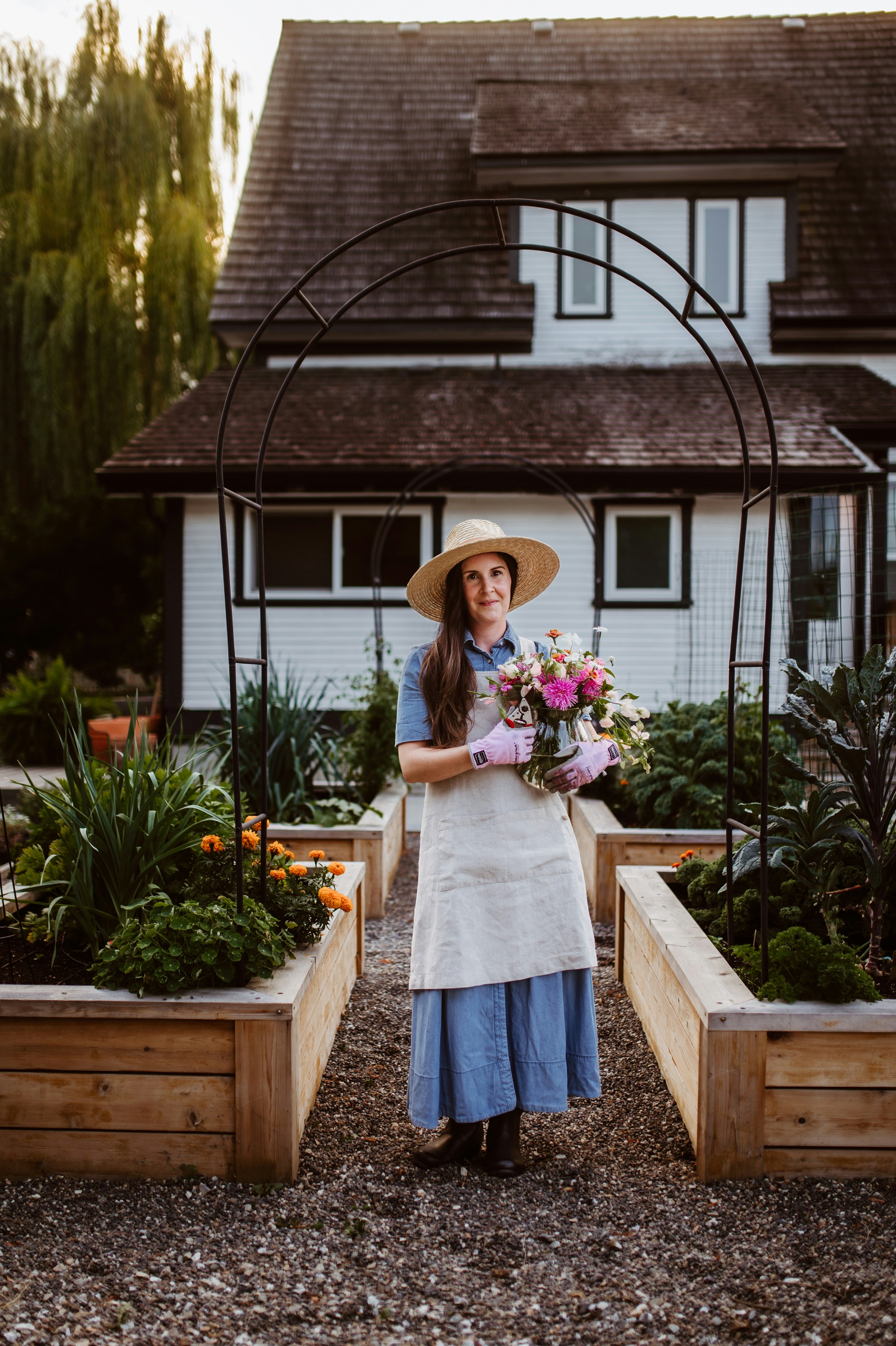Una mujer de pie frente a una casa sosteniendo un ramo de flores