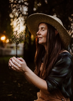 A woman in a hat holding a small plant