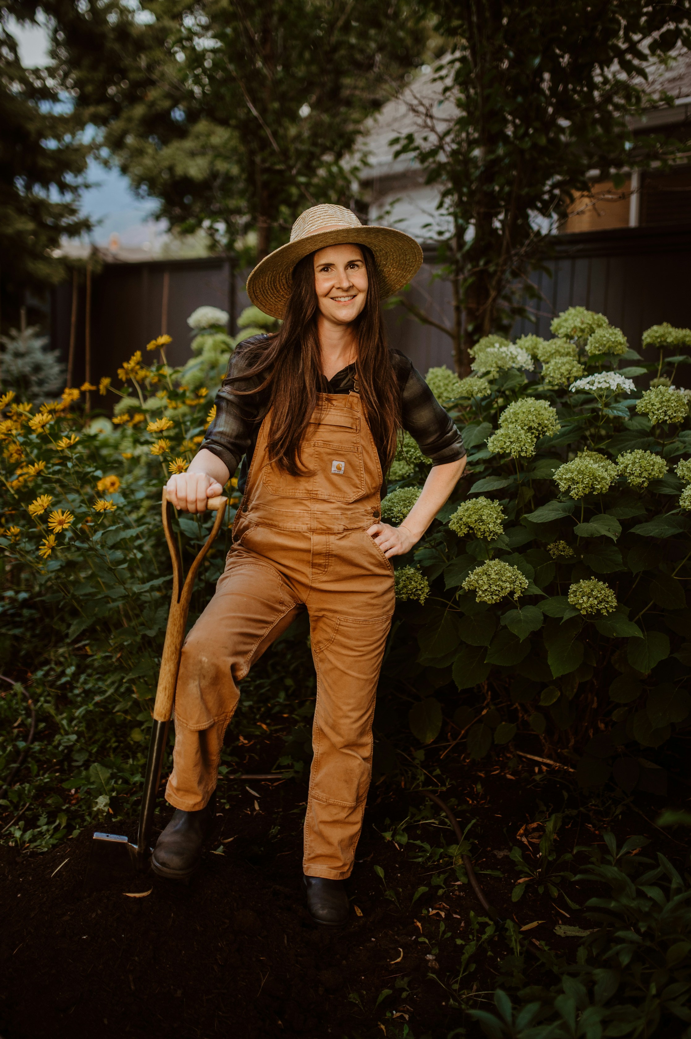 A woman in a hat and overalls posing for a picture