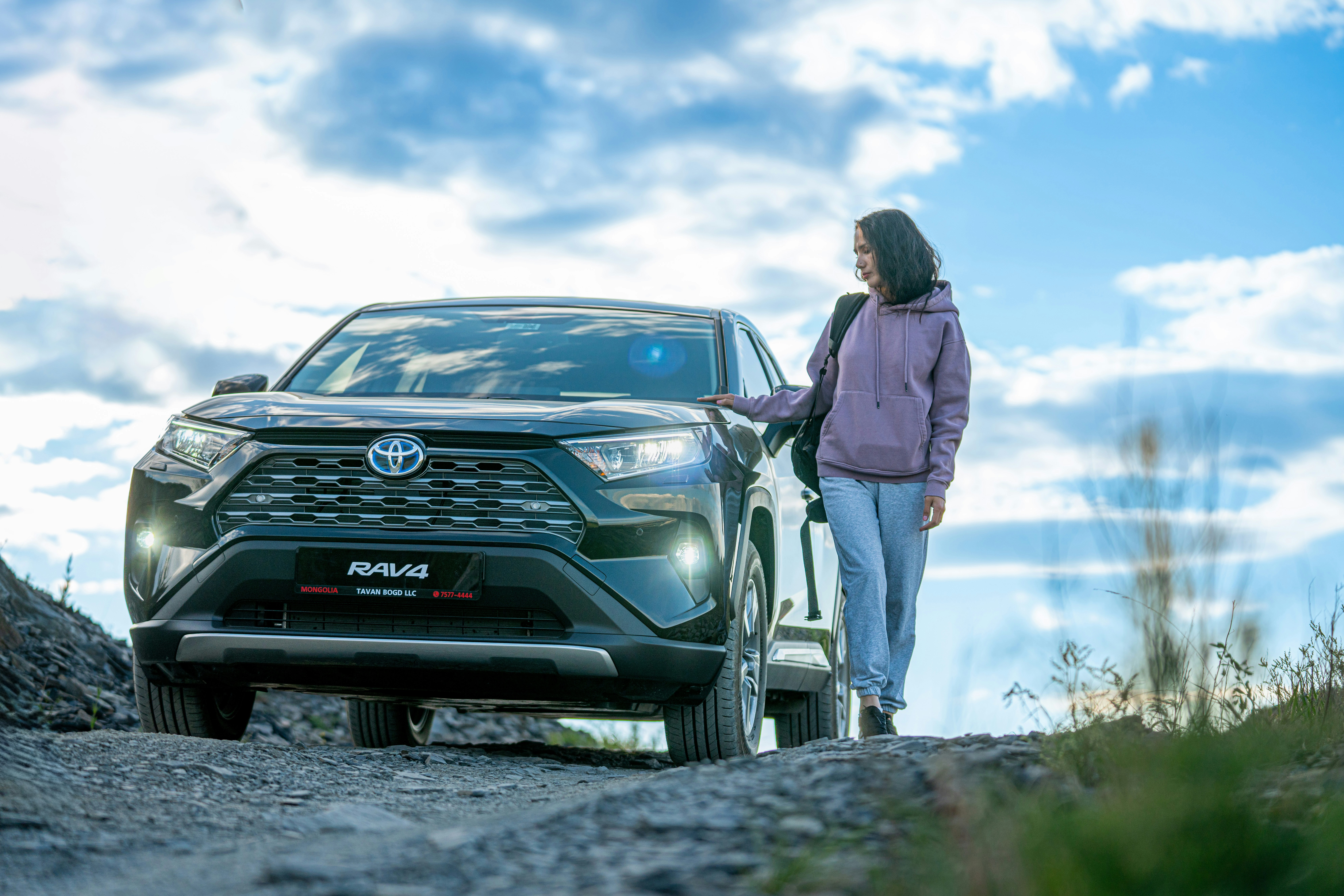 A woman standing next to a car on a dirt road