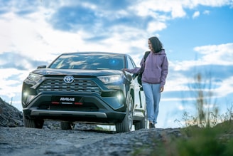 A woman standing next to a car on a dirt road