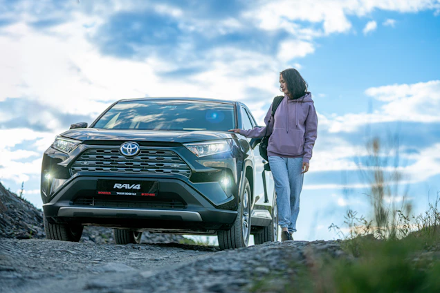 A woman standing next to a car on a dirt road