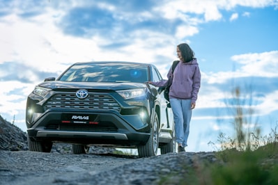 A woman standing next to a car on a dirt road