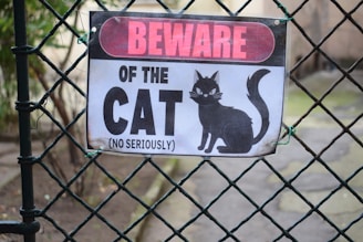 A sign on a fence that says beware of the cat