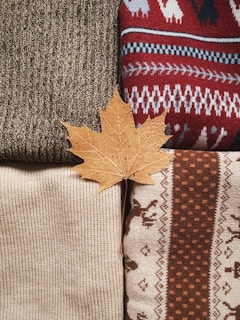 A maple leaf laying on a pile of sweaters
