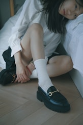 A woman sitting on a bed wearing black shoes