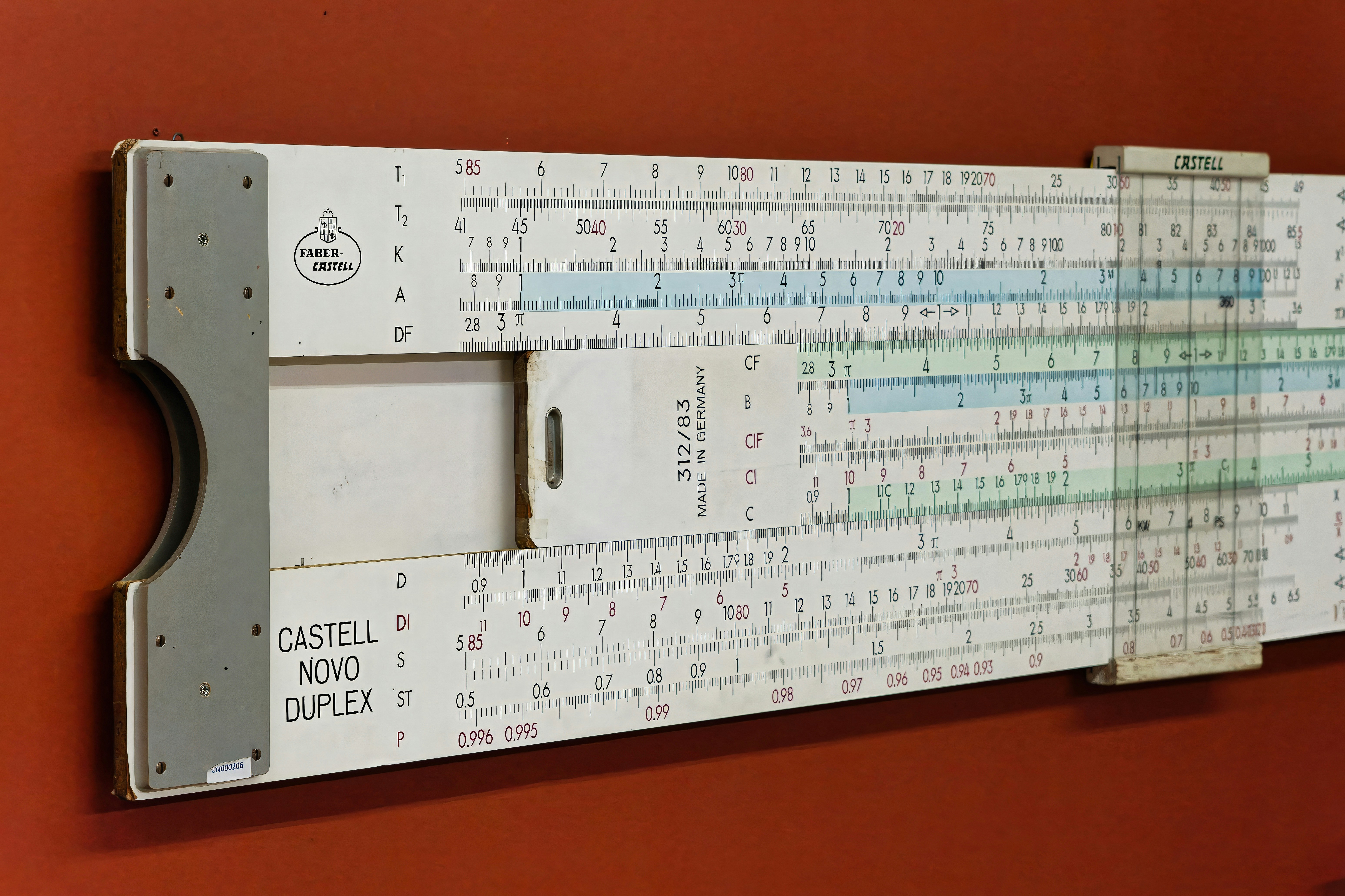 Vintage slide rule from the early 20th century displayed on a wall, showcasing mathematical calculations and engineering design - A vintage slide rule rests against a rust-colored wall, revealing scales and markings used for mathematical calculations in engineering during the 20th century.