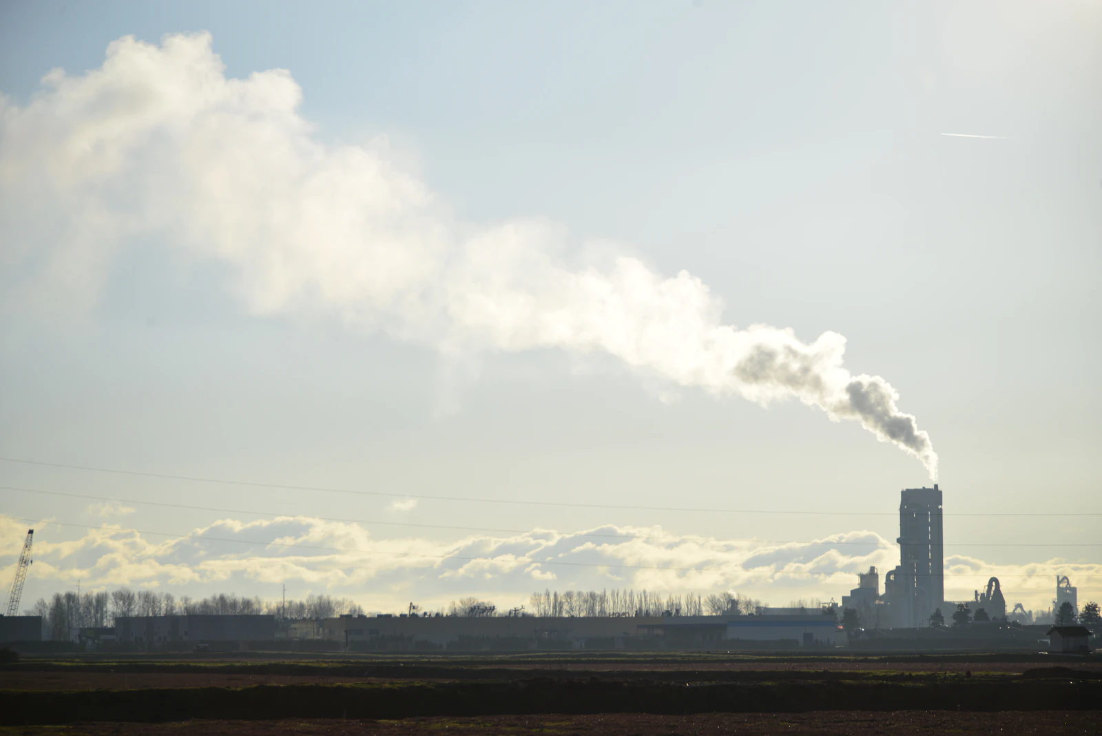 Cement plant releasing a plume of exhaust against a clear sky, one of the four sectors where Indian exporters face EU CBAM embedded emissions requirements