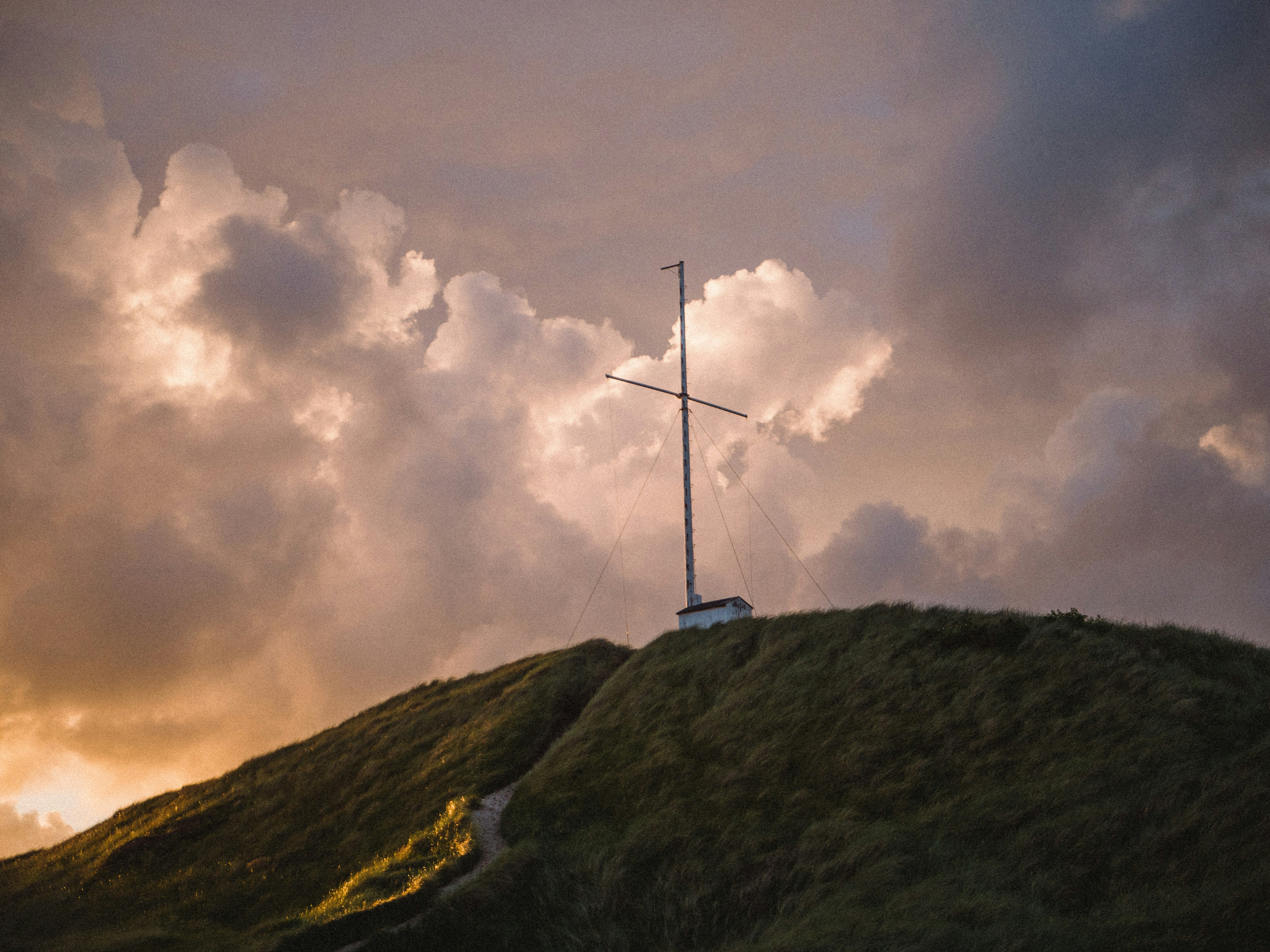 A cross on top of a hill under a cloudy sky