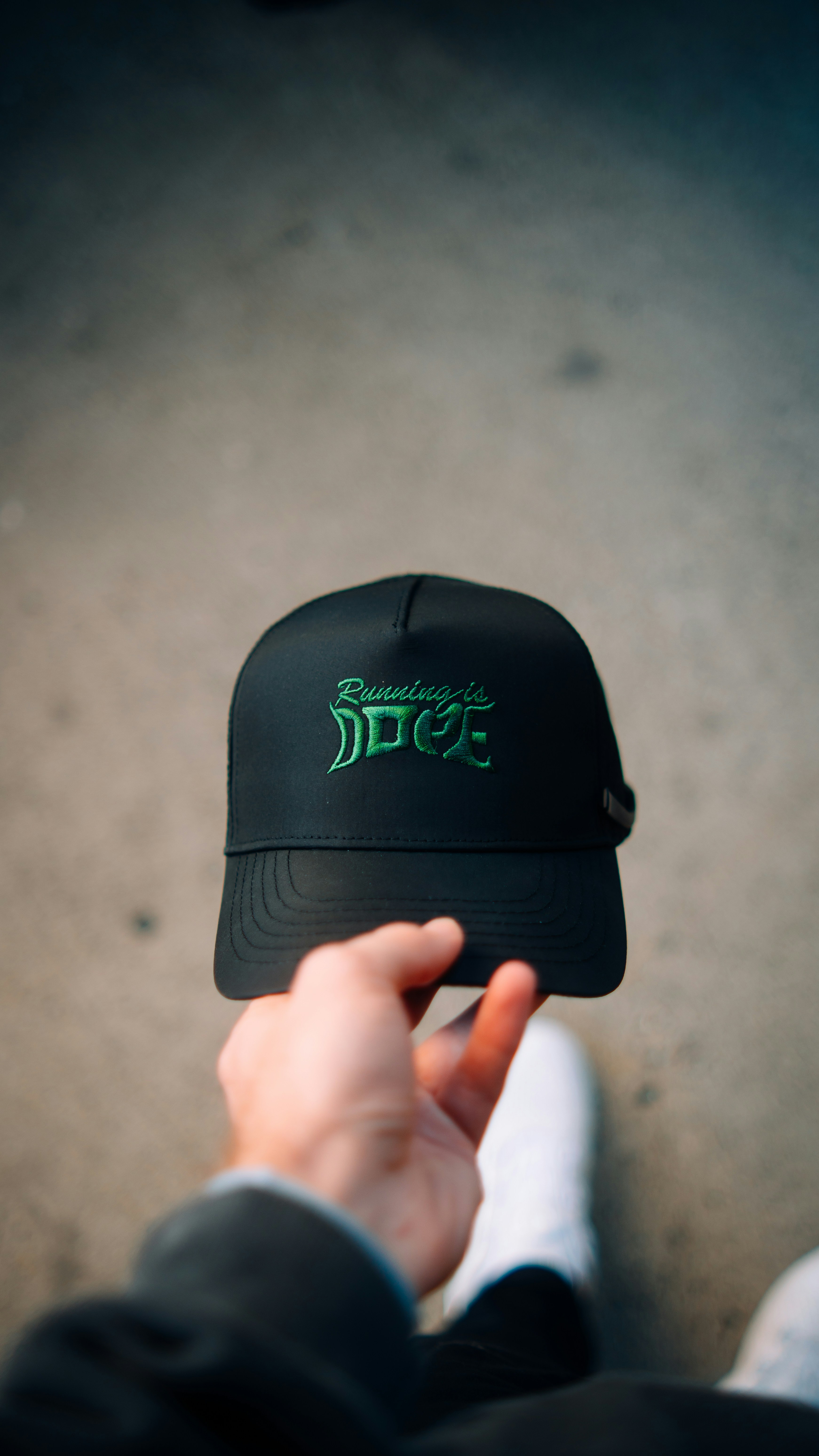 A person holding a black hat with green lettering