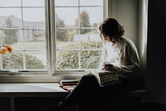 A woman sitting on a window sill reading a book