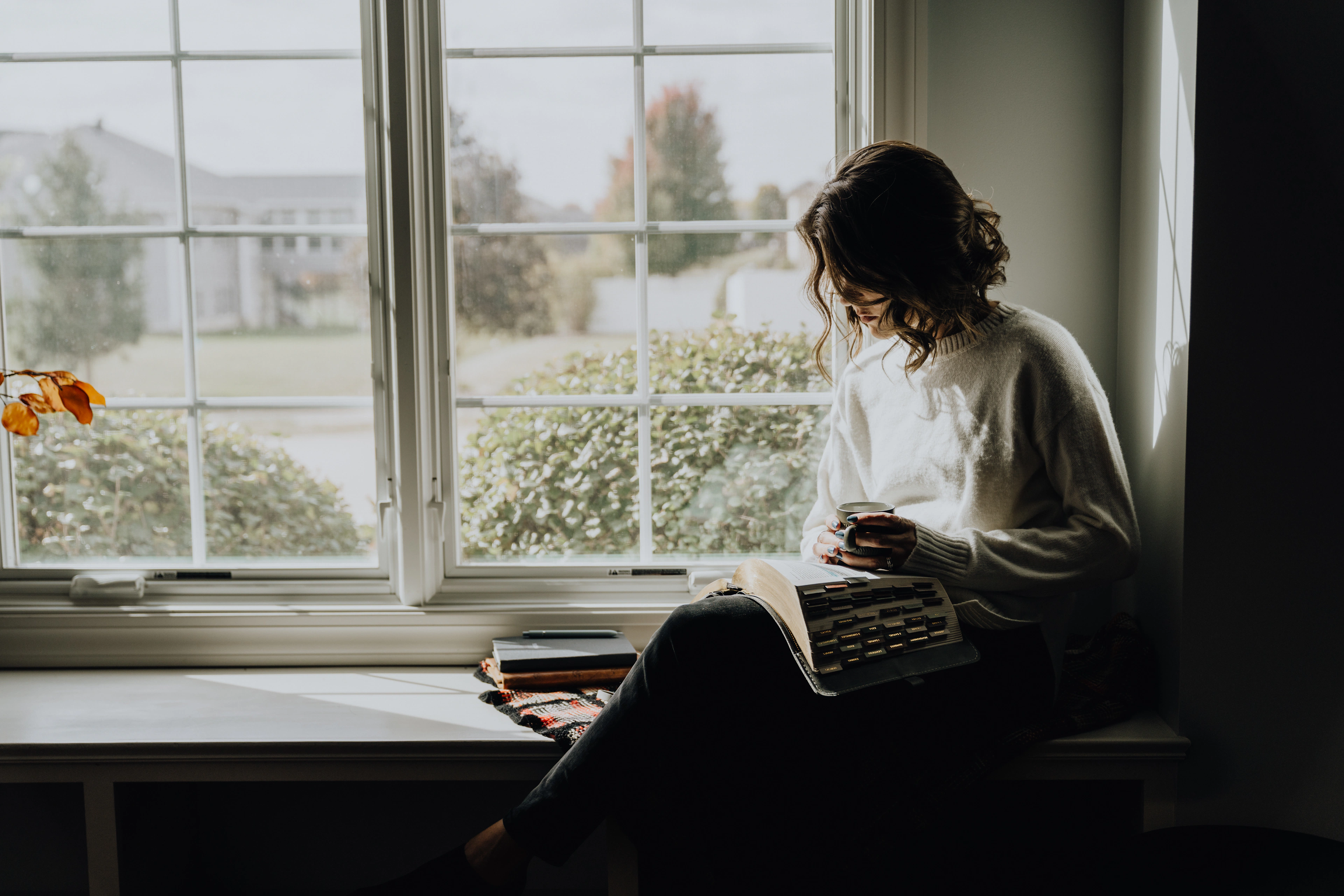 A woman reading with a mug by the window