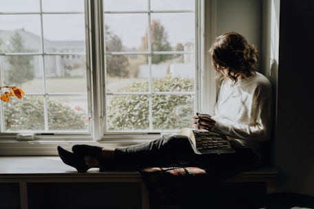 A woman sitting on a window sill reading a book