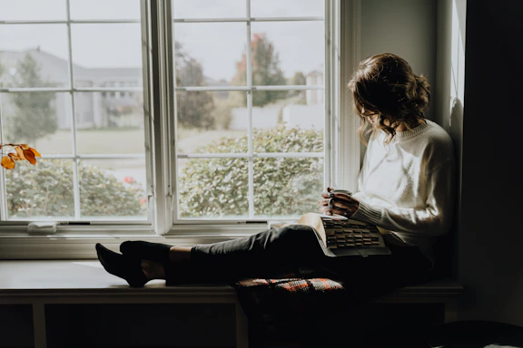 A woman sitting on a window sill reading a book