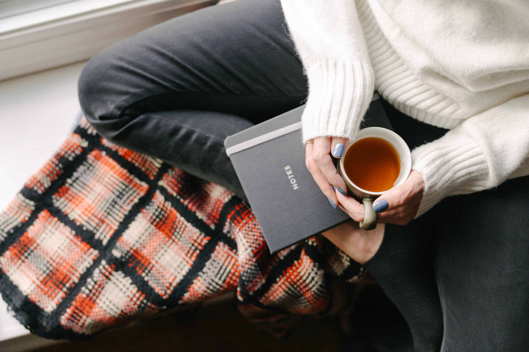 Une femme assise sur un rebord de fenêtre tient une tasse de thé, ambiance cosy et paisible