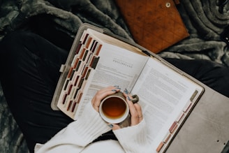 A person is holding a cup of tea and reading a book
