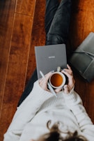 A person sitting on the floor with a laptop and a cup of coffee