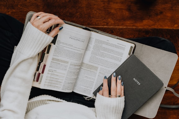 A woman reading a book while holding a laptop