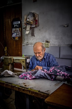 An old man sitting at a table working on a sewing machine