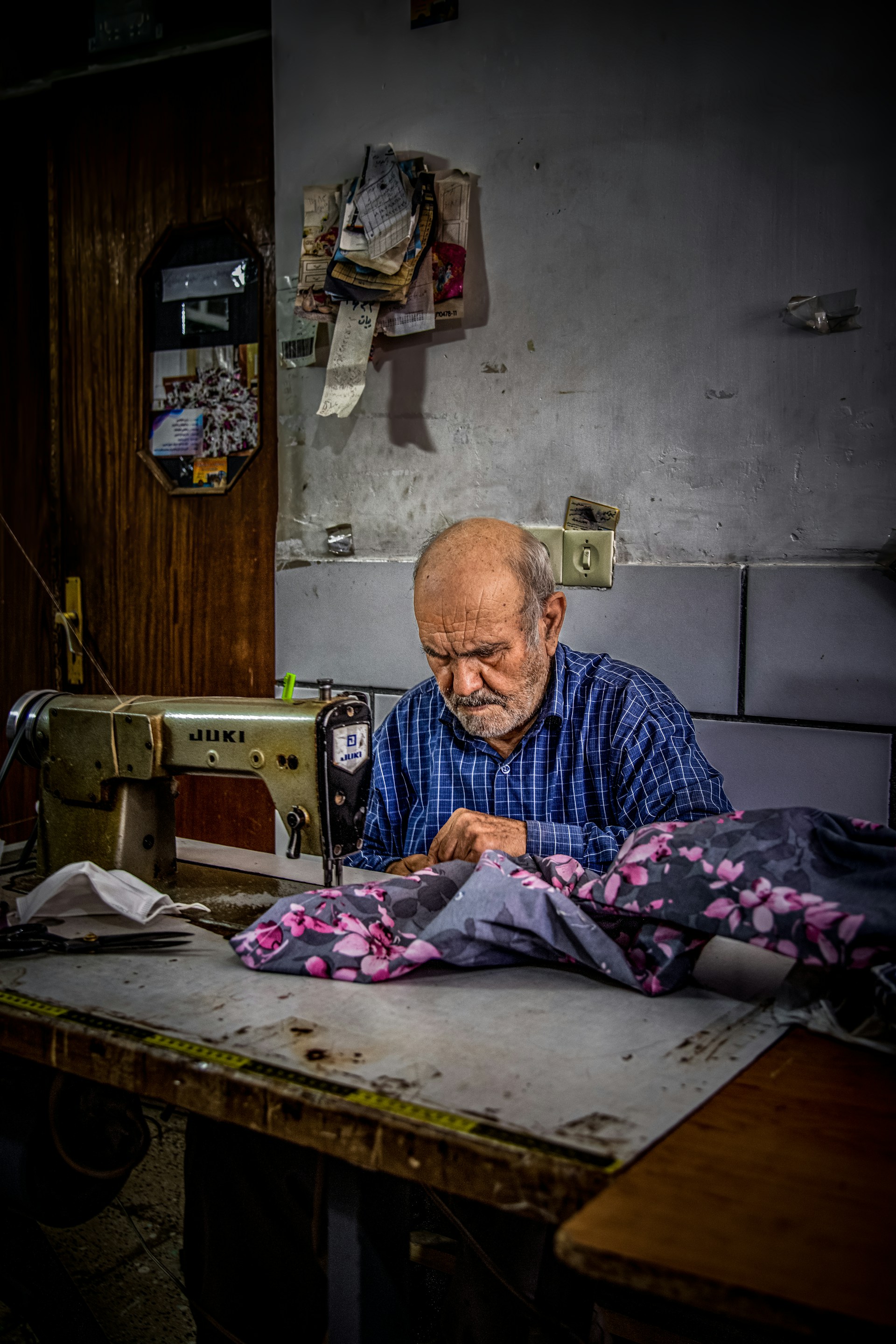 An old man sitting at a table working on a sewing machine