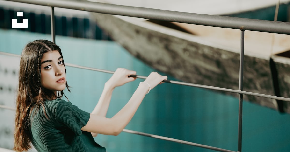 A woman is sitting on a railing near a body of water photo – Free Girl ...