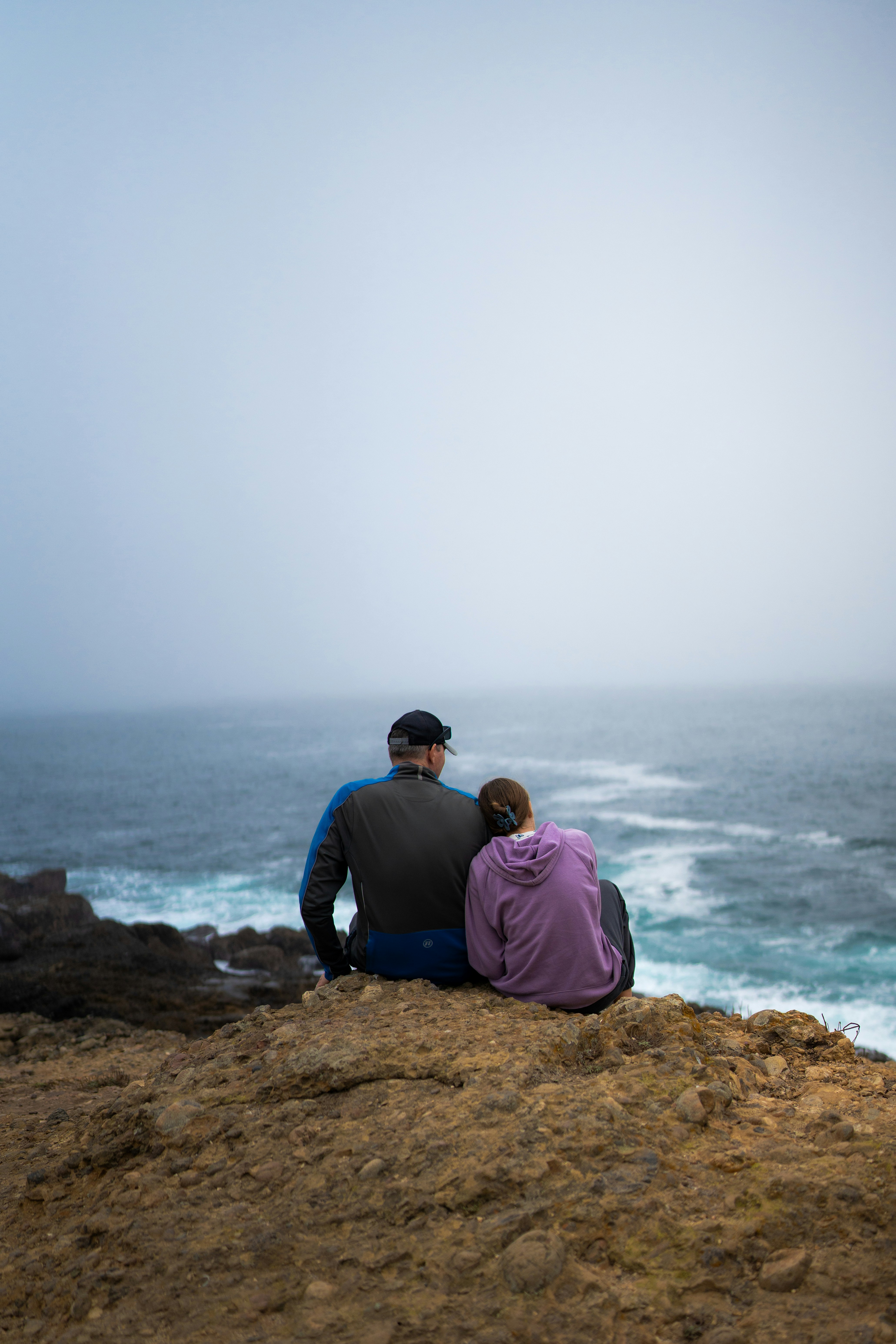 A couple of people sitting on top of a cliff photo – Free Beach Image ...