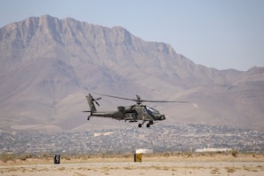 A helicopter flying over a desert with a mountain in the background