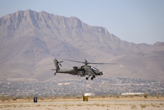 A helicopter flying over a desert with a mountain in the background
