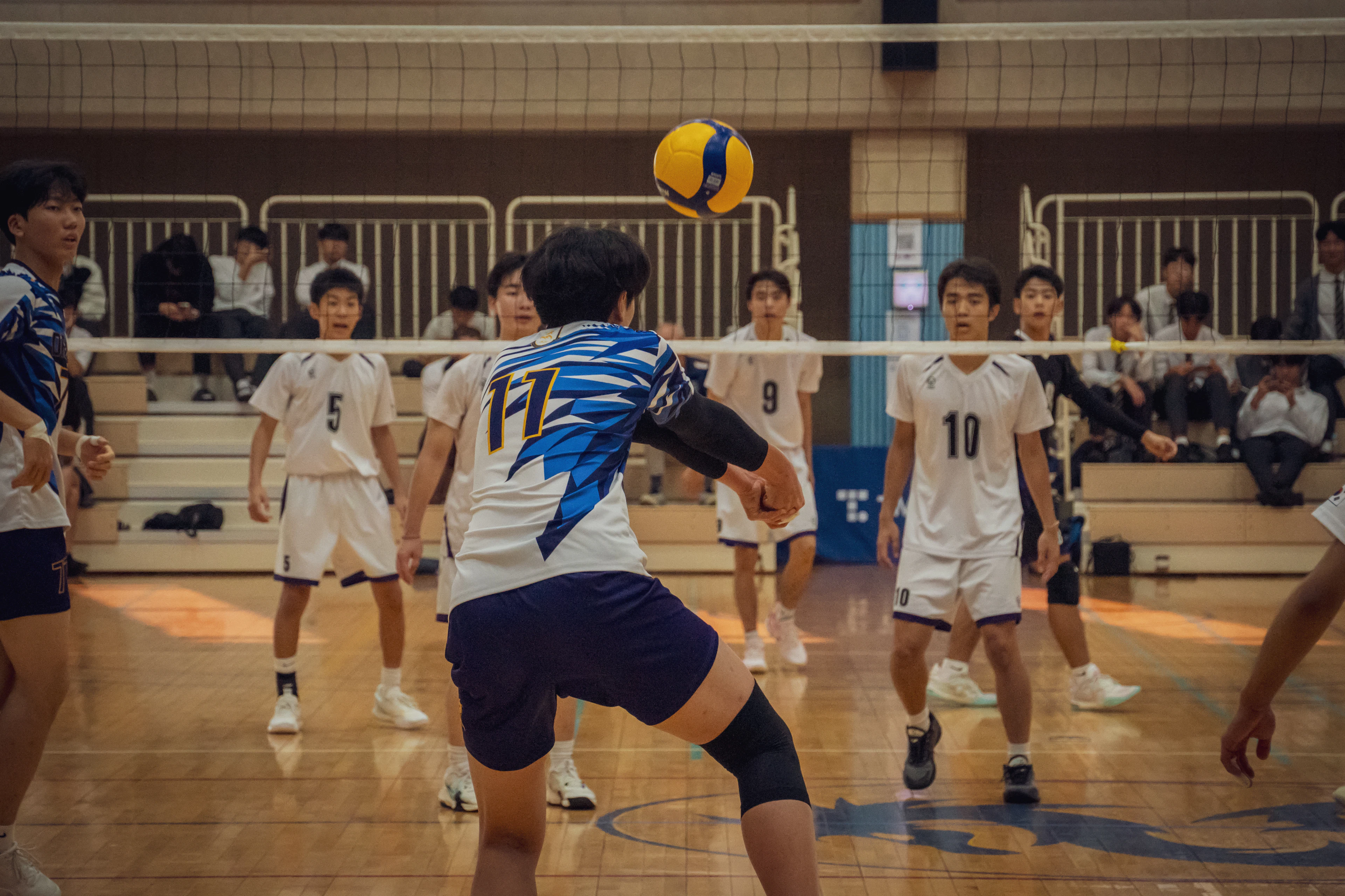 Young men's volleyball team playing a match in a school gymnasium