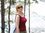 A woman in a red shirt and sunglasses walking in the woods