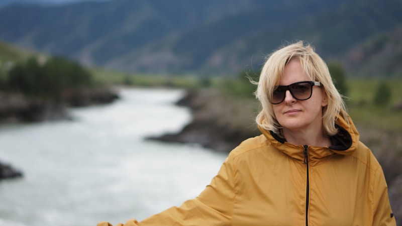 Attraktive Frau in gelber Jacke und Sonnenbrille am Fluss