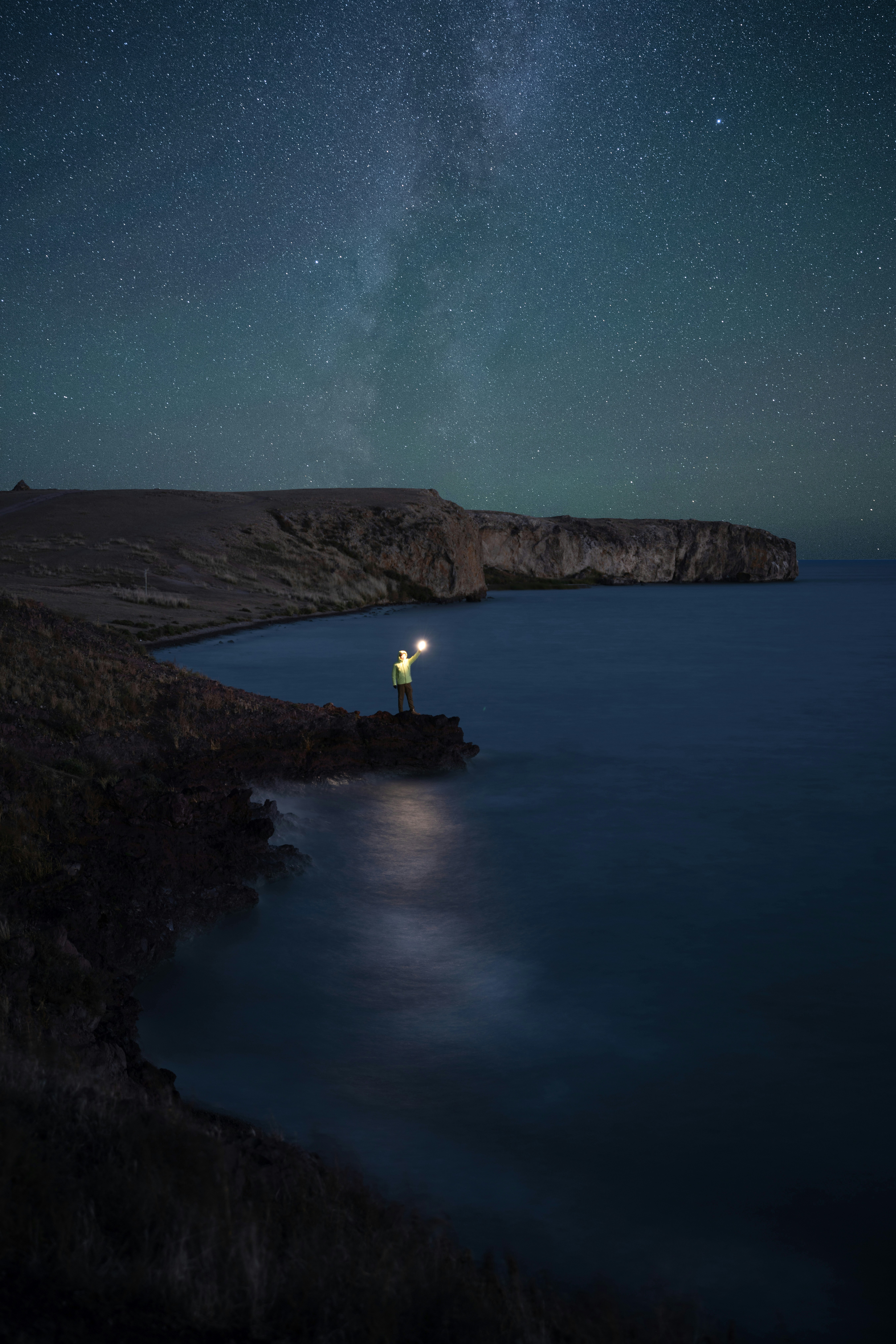 A person standing on a cliff looking at the night sky