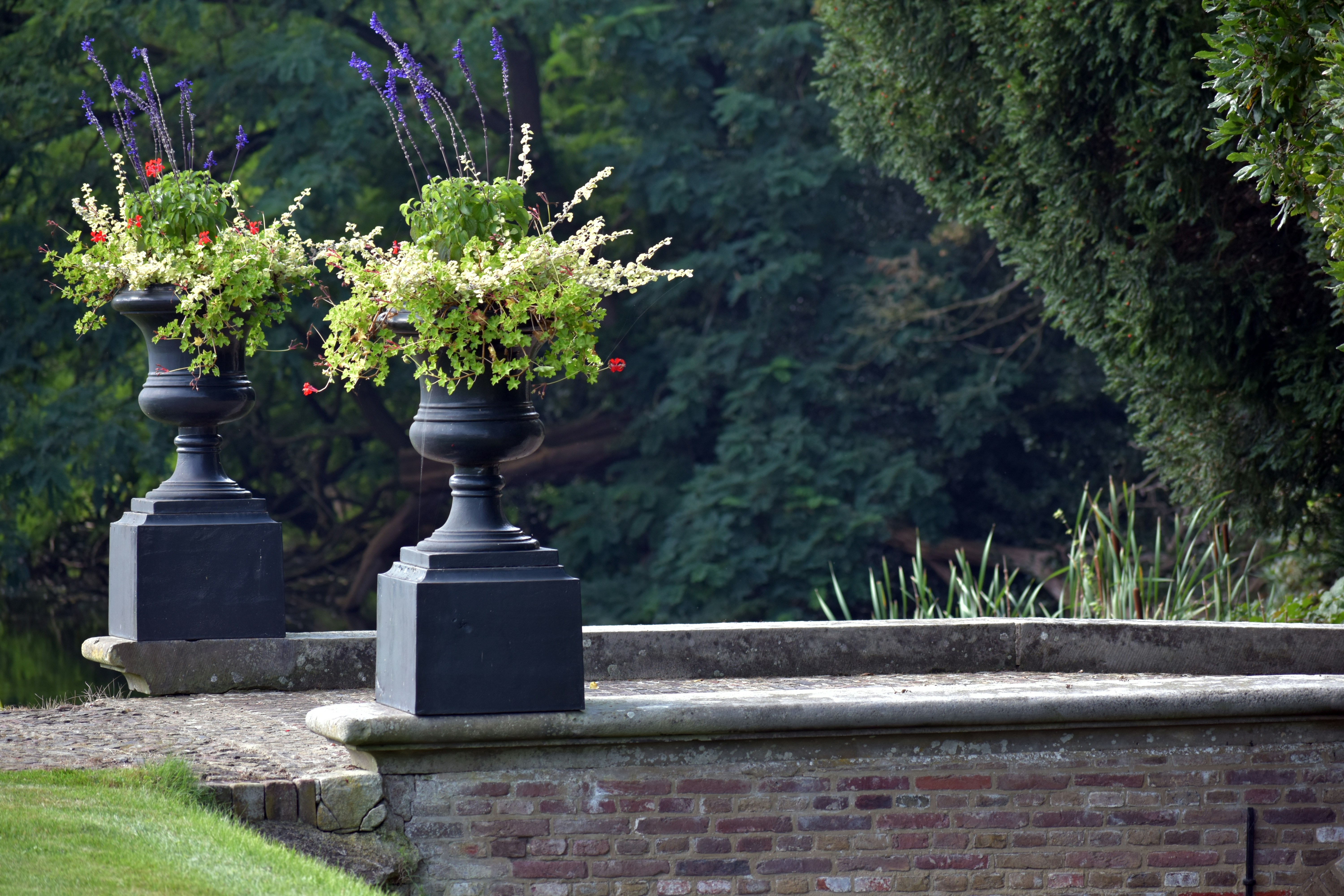 A couple of black vases filled with flowers on top of a stone wall