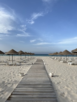 A wooden walkway leading to a beach with umbrellas