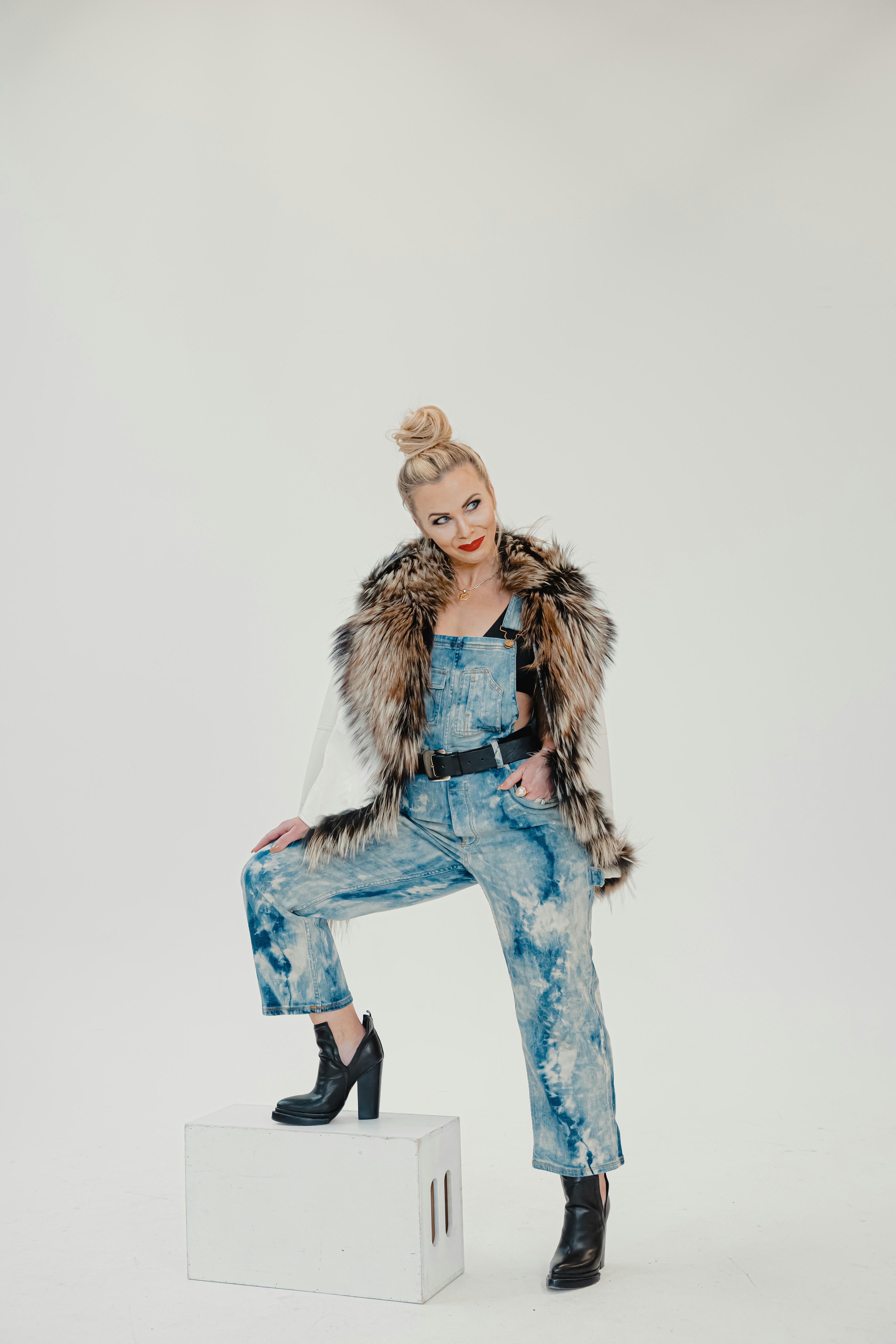 A woman in overalls and a fur vest sitting on top of a white box