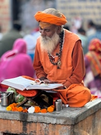 A man with a long white beard and orange turban is sitting on a