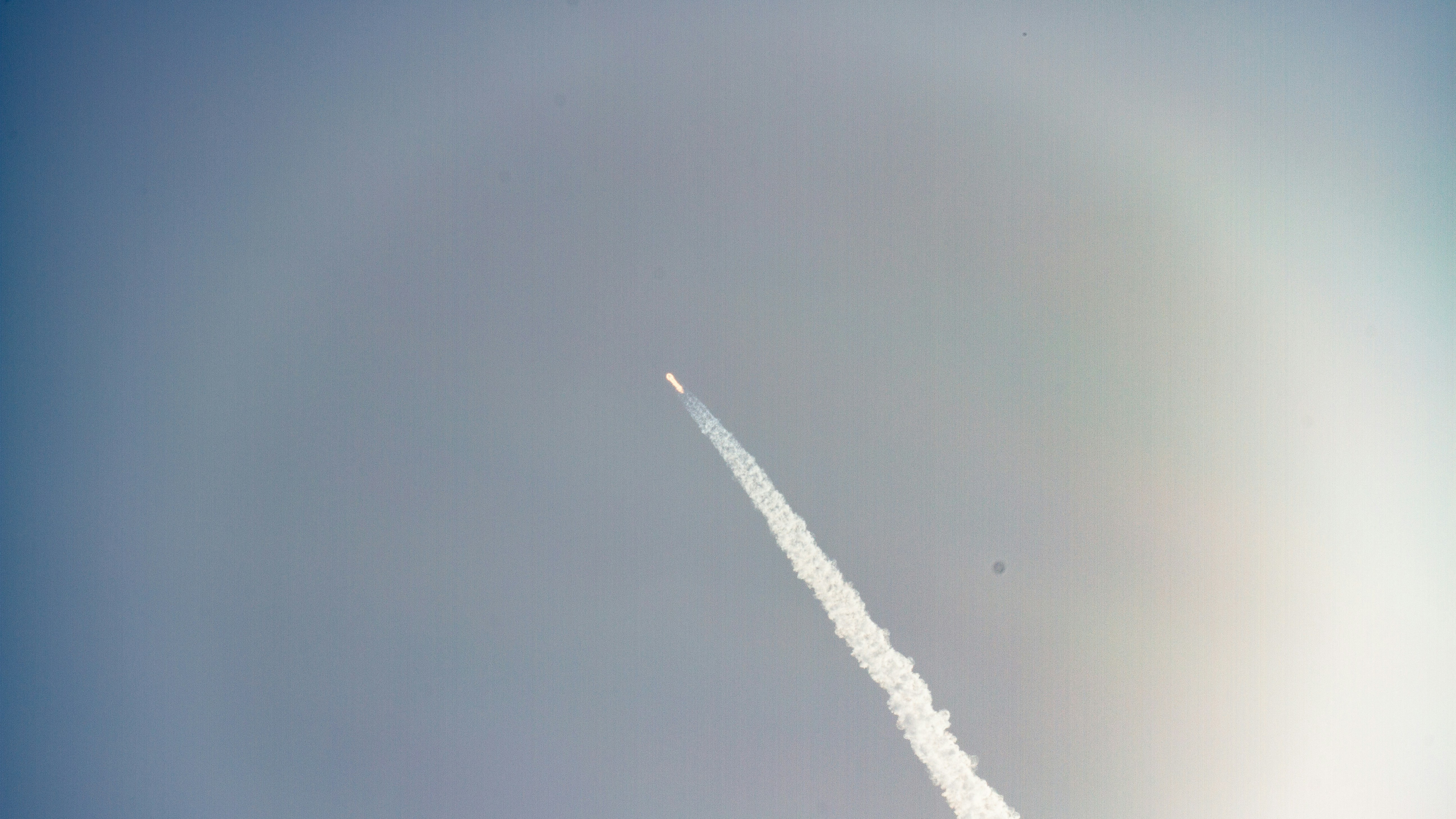 Cohete espacial despegando con estela de fuego y humo blanco contra cielo azul