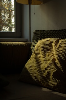 A bed with a yellow blanket on it next to a window