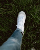 A person standing in the grass wearing white sneakers