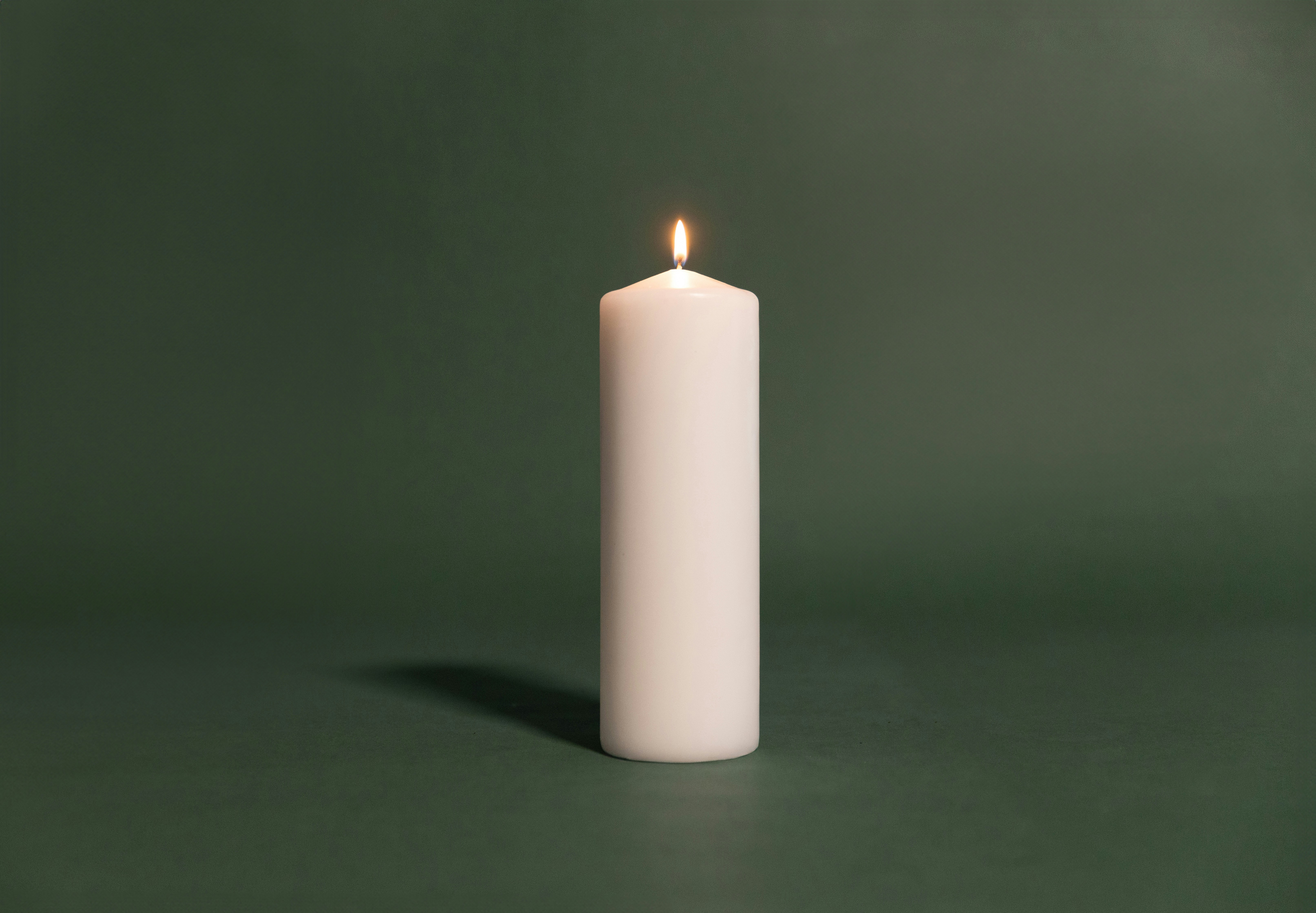 A single white candle on a green surface