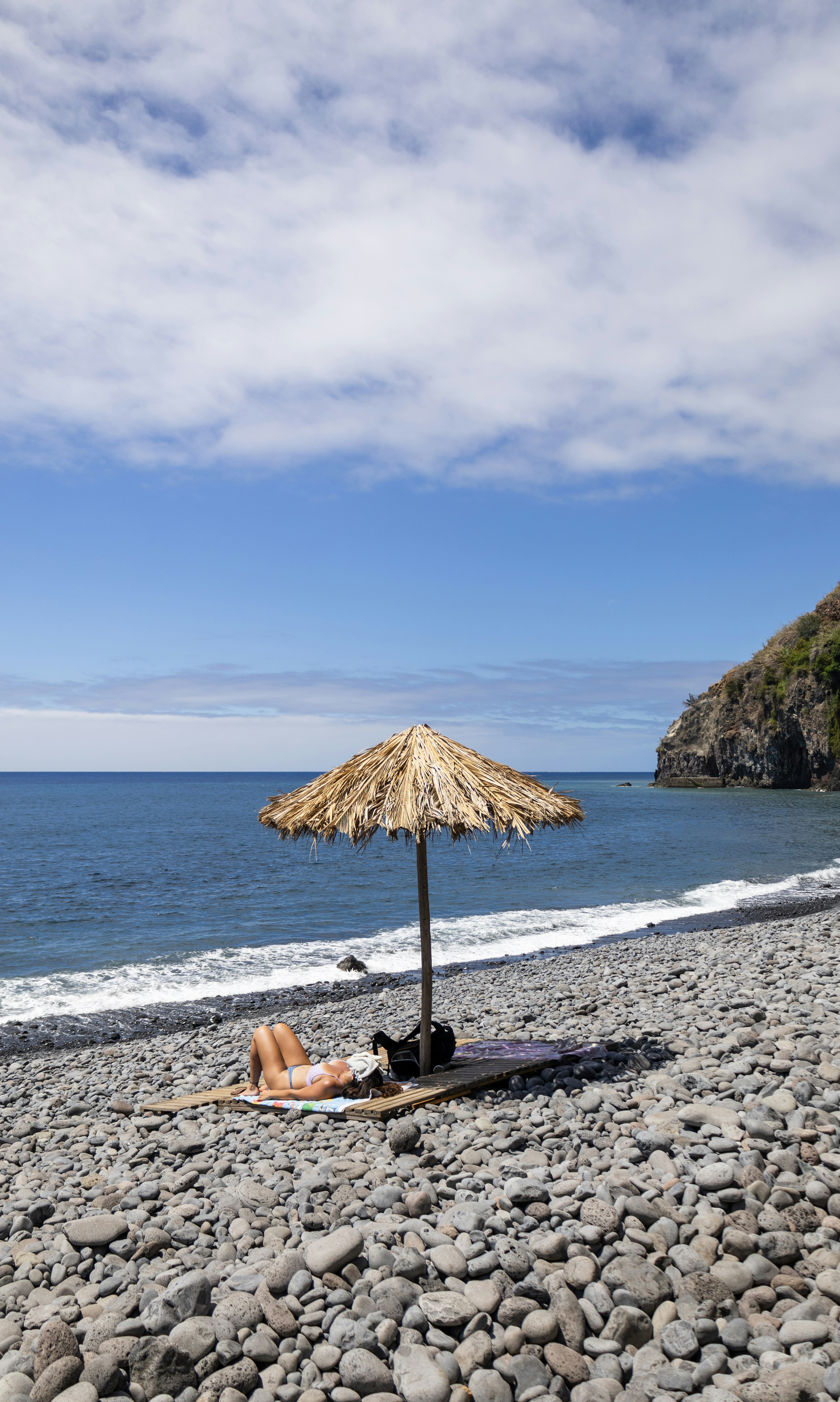 A woman laying on a beach under a straw umbrella